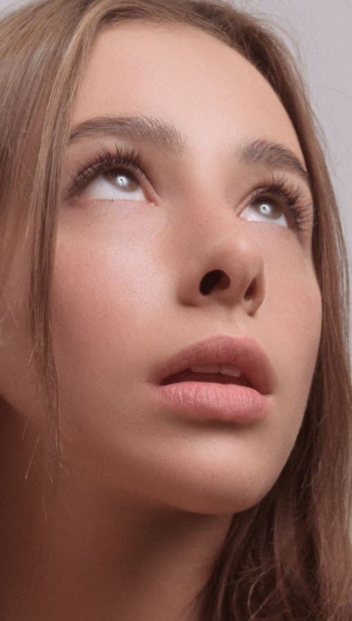A young woman with warm tan skin looking upward in soft light.